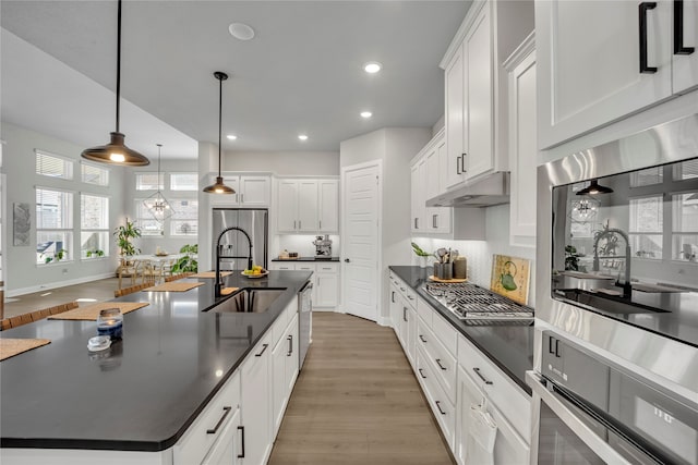 kitchen with white cabinetry, pendant lighting, sink, hardwood / wood-style floors, and a kitchen island with sink