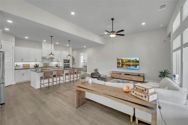 living room with ceiling fan, sink, and light wood-type flooring