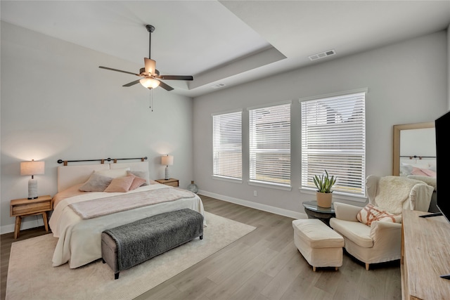 bedroom featuring ceiling fan, a raised ceiling, and light hardwood / wood-style flooring