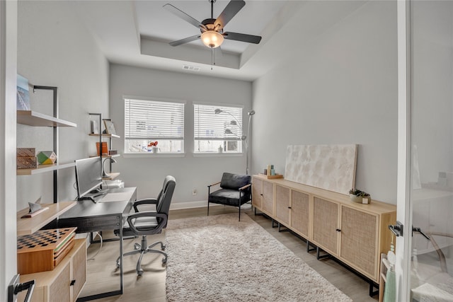 office space with ceiling fan, light wood-type flooring, and a tray ceiling