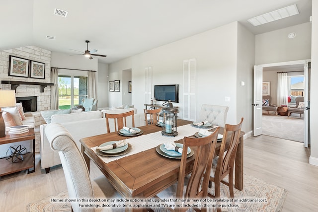 dining area featuring a stone fireplace, light hardwood / wood-style flooring, ceiling fan, and vaulted ceiling