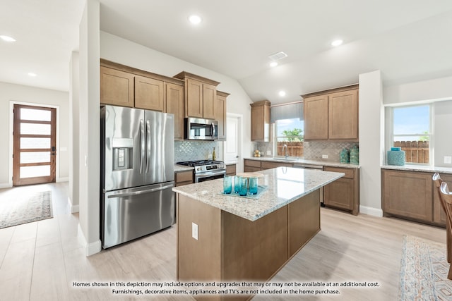 kitchen with stainless steel appliances, light hardwood / wood-style floors, light stone countertops, lofted ceiling, and a kitchen island