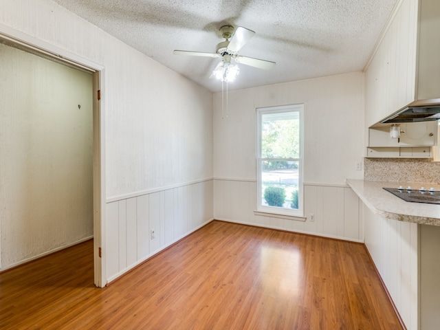 unfurnished dining area featuring light wood-type flooring, a textured ceiling, and ceiling fan