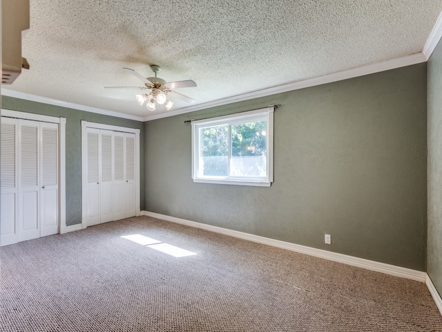 unfurnished bedroom with multiple closets, a textured ceiling, carpet flooring, and ceiling fan