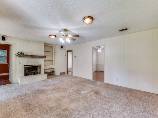 unfurnished living room with carpet, a fireplace, a textured ceiling, wooden walls, and ceiling fan