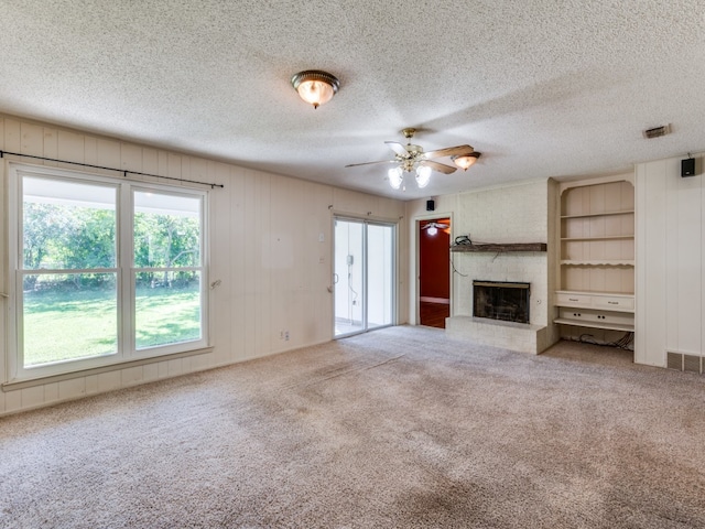 unfurnished living room featuring a large fireplace, a wealth of natural light, carpet floors, and ceiling fan