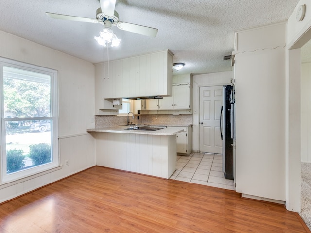 kitchen with kitchen peninsula, stainless steel refrigerator, a healthy amount of sunlight, and light hardwood / wood-style flooring