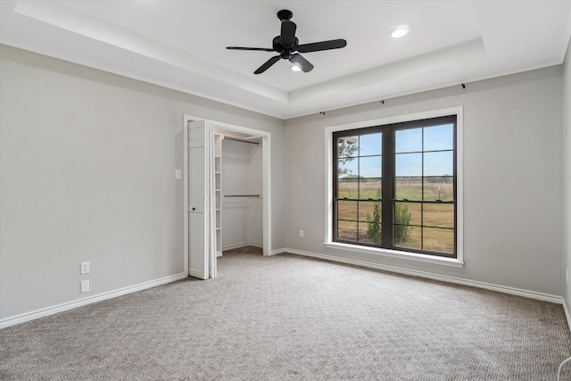 unfurnished bedroom with a closet, a tray ceiling, carpet flooring, and ceiling fan