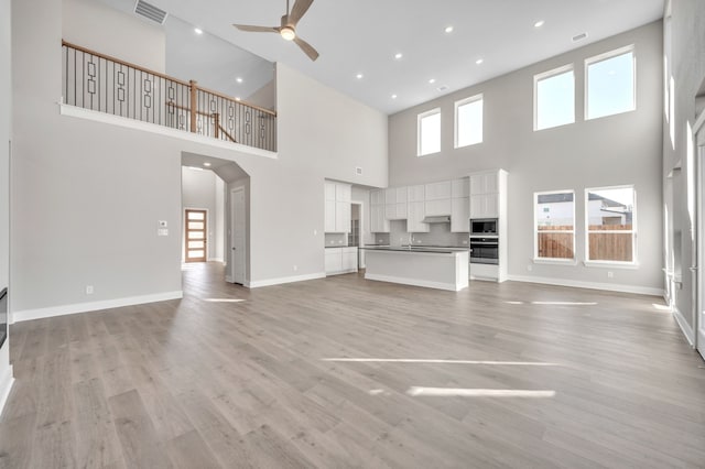 unfurnished living room with ceiling fan, a towering ceiling, and light wood-type flooring