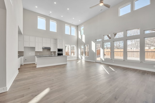 unfurnished living room featuring ceiling fan, a towering ceiling, sink, and light hardwood / wood-style flooring