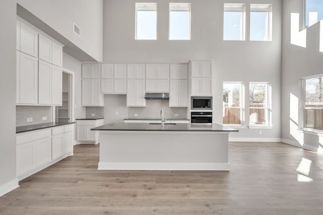 kitchen with built in microwave, a towering ceiling, oven, and white cabinets