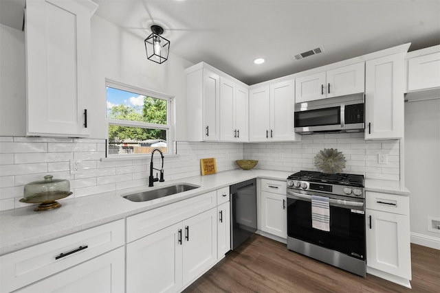 kitchen with appliances with stainless steel finishes, white cabinetry, sink, light stone counters, and dark wood-type flooring