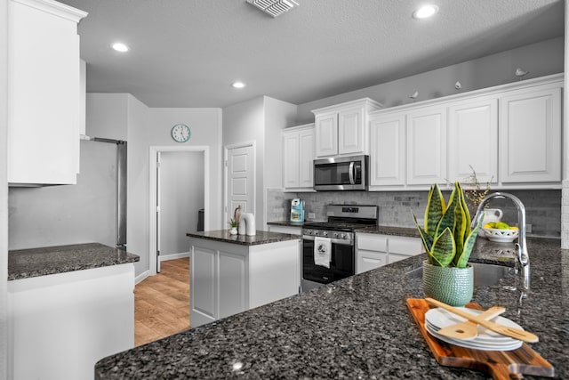 kitchen featuring stainless steel appliances, dark stone counters, white cabinetry, light hardwood / wood-style floors, and a center island