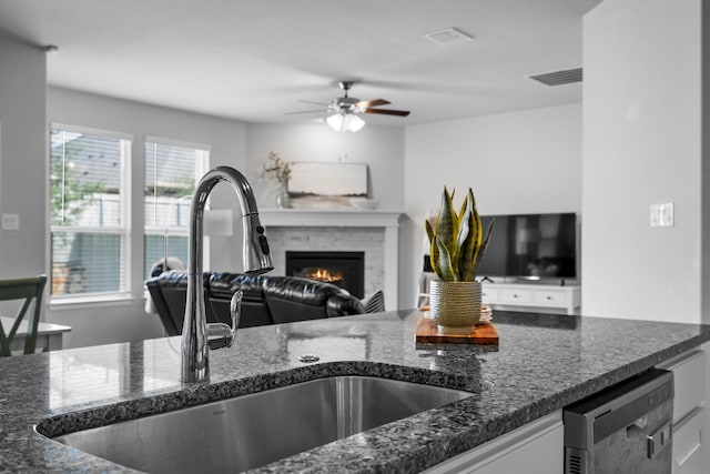 2614 Cowbird Way, Northlake, TX 76247 - kitchen with open floor plan, dark stone counters, a ceiling fan, a warm lit fireplace, and stainless steel dishwasher