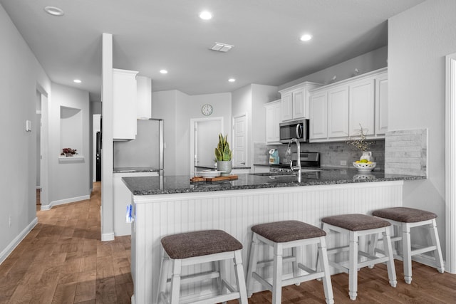 kitchen featuring dark stone counters, white cabinets, kitchen peninsula, hardwood / wood-style flooring, and appliances with stainless steel finishes