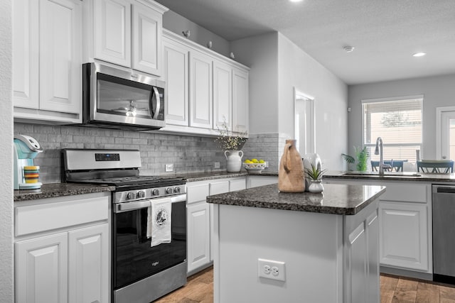 2614 Cowbird Way, Northlake, TX 76247 - kitchen with appliances with stainless steel finishes, a center island, decorative backsplash, light wood-type flooring, and white cabinetry