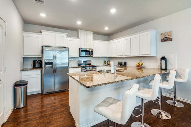 kitchen with stainless steel appliances, white cabinets, kitchen peninsula, decorative backsplash, and dark hardwood / wood-style floors