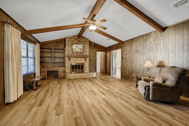 living room featuring a fireplace, light wood-type flooring, a textured ceiling, wooden walls, and ceiling fan