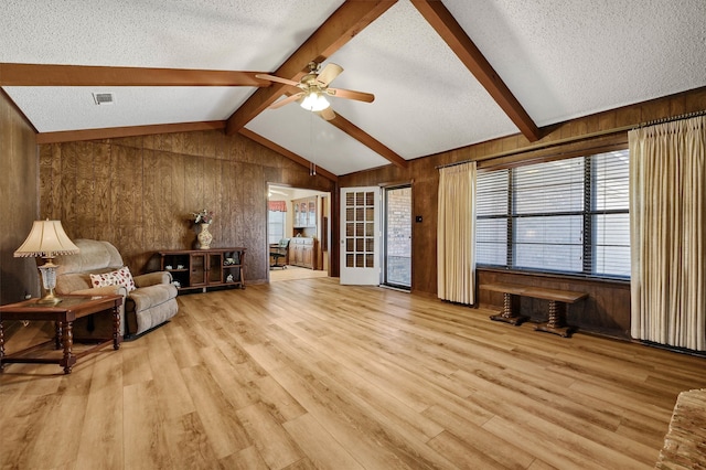 living area with lofted ceiling with beams, a textured ceiling, wood walls, ceiling fan, and light hardwood / wood-style flooring