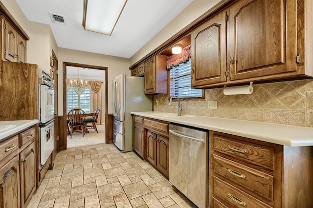 kitchen featuring tasteful backsplash, sink, stainless steel appliances, and an inviting chandelier