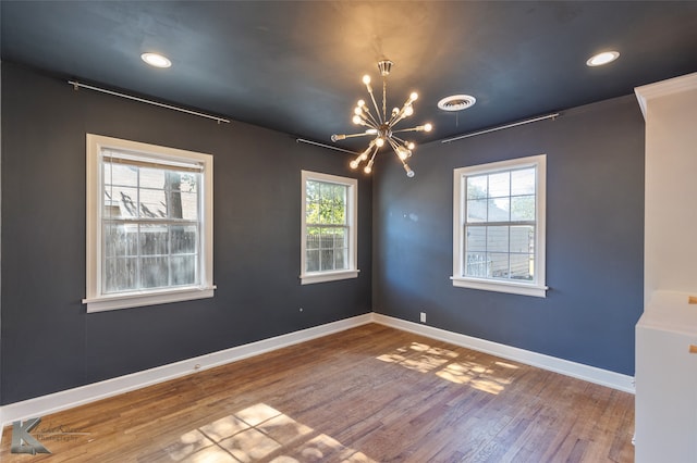 empty room featuring a wealth of natural light, wood-type flooring, and a notable chandelier