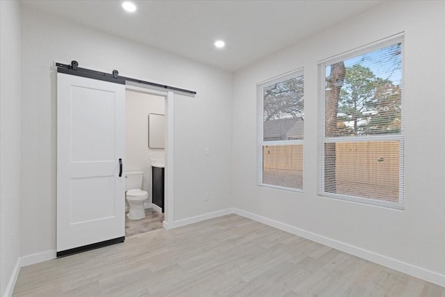 interior space with light hardwood / wood-style floors, a barn door, and ensuite bathroom