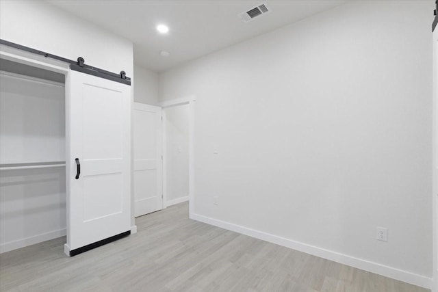 unfurnished bedroom with a barn door and light wood-type flooring