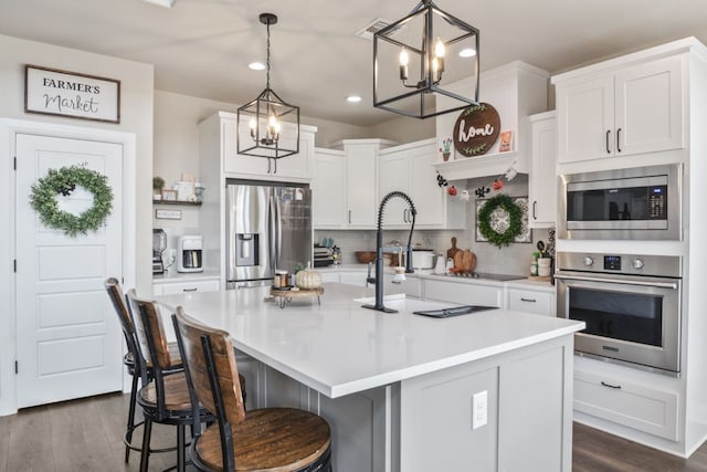 kitchen featuring white cabinets, appliances with stainless steel finishes, hanging light fixtures, and a kitchen island with sink