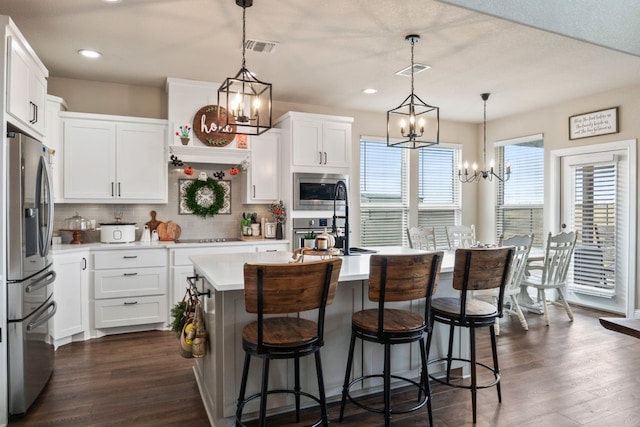 kitchen with white cabinets, appliances with stainless steel finishes, a center island with sink, and decorative light fixtures