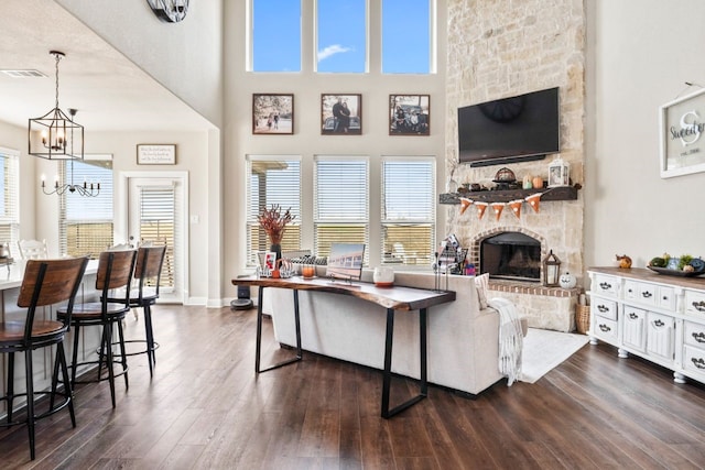 living room featuring a chandelier, a fireplace, dark hardwood / wood-style floors, and a high ceiling