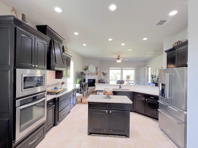 kitchen with custom range hood, stainless steel appliances, ceiling fan, sink, and a kitchen island