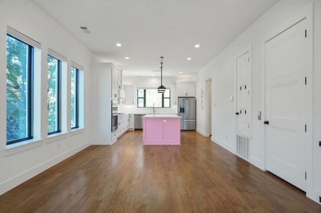 kitchen with appliances with stainless steel finishes, a healthy amount of sunlight, decorative light fixtures, and a kitchen island