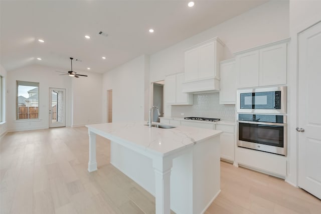 kitchen with built in microwave, stainless steel oven, an island with sink, and a sink