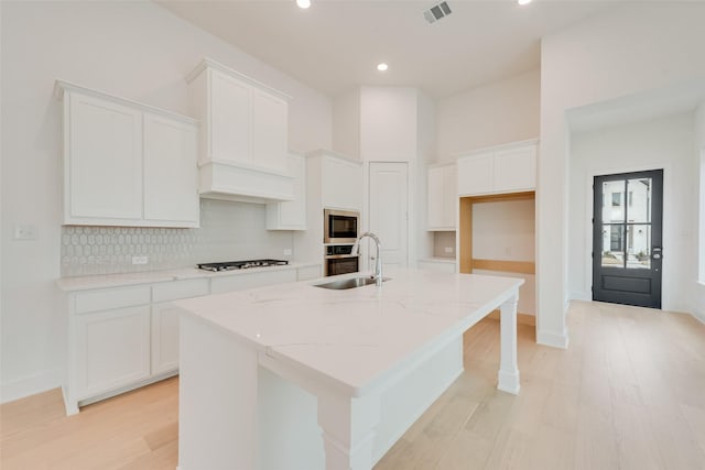 kitchen featuring black microwave, a kitchen island with sink, a sink, and white cabinetry