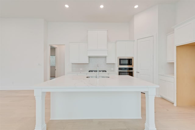 kitchen with white cabinets, stainless steel oven, an island with sink, light stone countertops, and black microwave