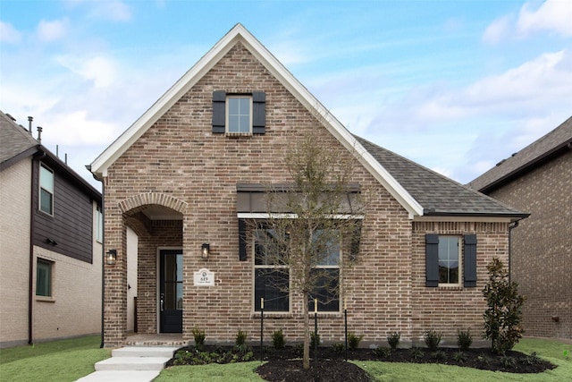 view of front of house featuring brick siding, roof with shingles, and a front lawn