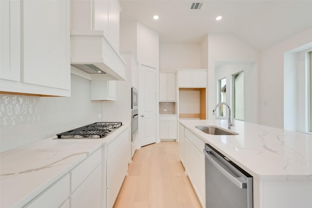 kitchen featuring stainless steel appliances, backsplash, white cabinets, a sink, and an island with sink