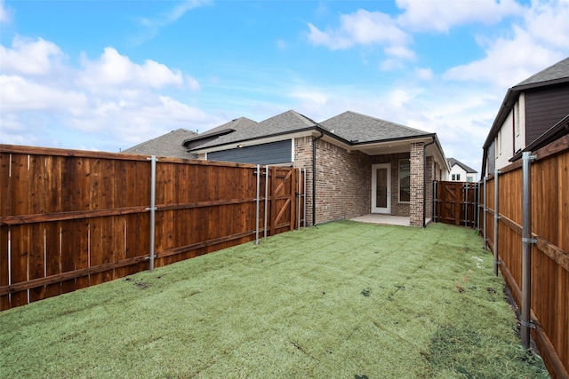 back of house featuring brick siding, a patio, a shingled roof, a lawn, and a fenced backyard