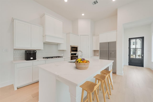 kitchen with stainless steel appliances, a kitchen island with sink, and white cabinets