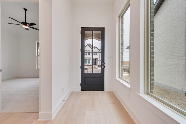 foyer featuring a ceiling fan, baseboards, plenty of natural light, and light wood finished floors