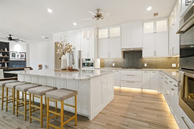 kitchen with light stone counters, a kitchen island, white cabinets, light wood-type flooring, and high end fridge