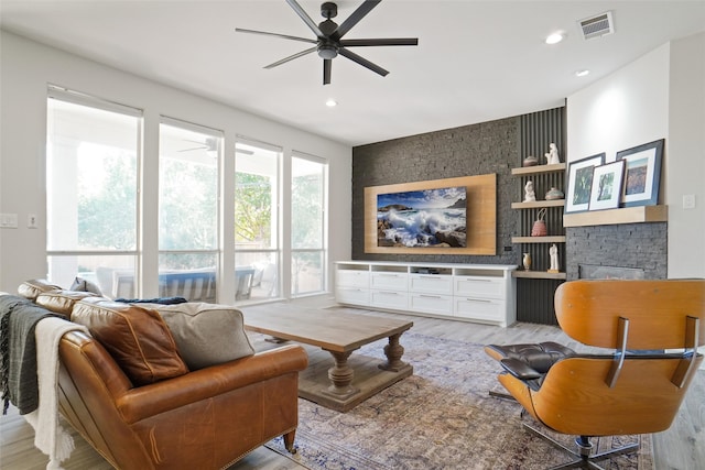 living room with a stone fireplace, light hardwood / wood-style flooring, and ceiling fan