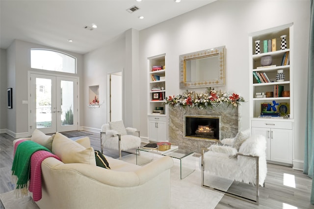 living room with built in features, french doors, a towering ceiling, a fireplace, and light hardwood / wood-style floors