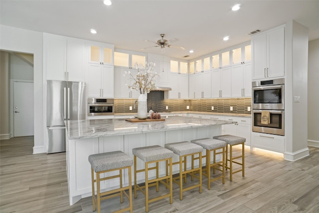 kitchen featuring a large island, stainless steel appliances, white cabinets, and light hardwood / wood-style flooring