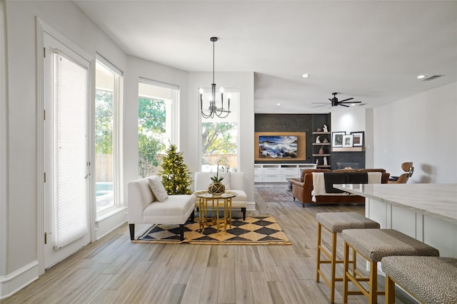 dining area featuring light wood-type flooring, ceiling fan with notable chandelier, and a fireplace