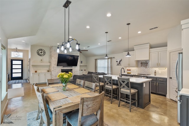 dining area featuring ceiling fan, a stone fireplace, and high vaulted ceiling