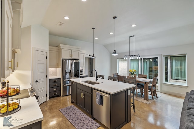 kitchen featuring lofted ceiling, sink, decorative light fixtures, stainless steel appliances, and a kitchen island with sink