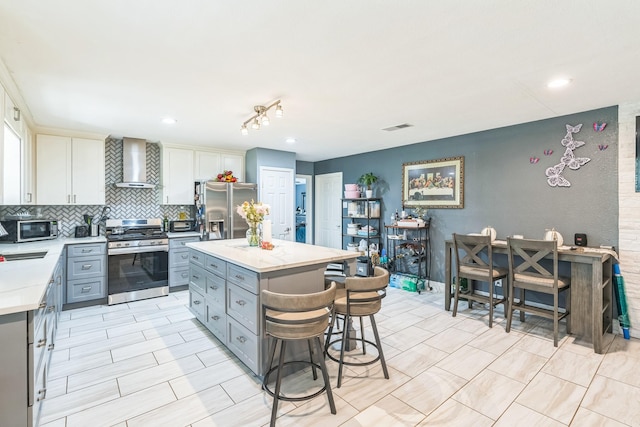 kitchen featuring stainless steel appliances, a kitchen island, white cabinetry, wall chimney range hood, and backsplash