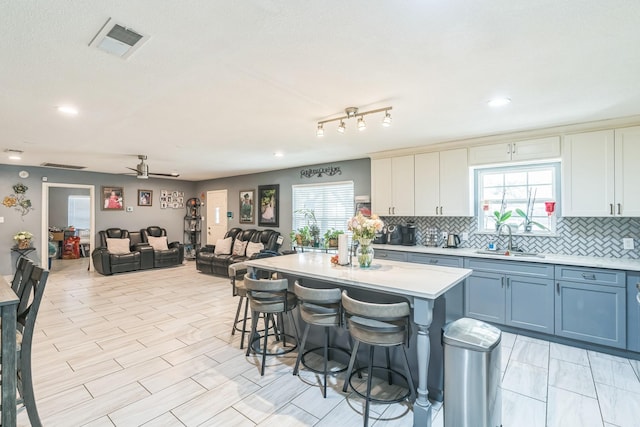 kitchen with a kitchen breakfast bar, a center island, ceiling fan, sink, and white cabinetry