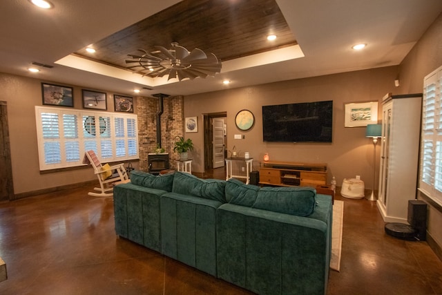 living room with a tray ceiling, a wood stove, and ceiling fan